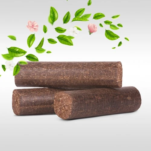 Three cylindrical brown biofuel briquettes stacked on a light gradient background, with green leaves and pink flowers above.